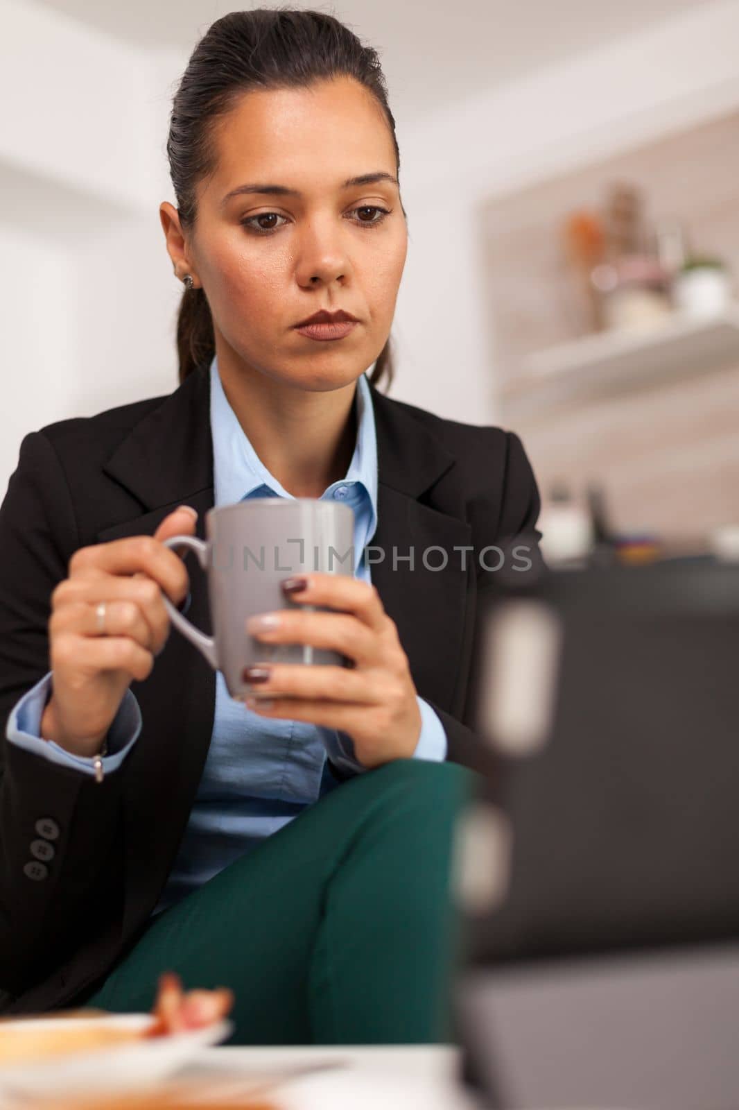 Portret of business woman watching on tablet and drinking a cup of coffee. Freelancer reading the last news online before going to work, using modern technology in the kitchen while eating a healthy meal