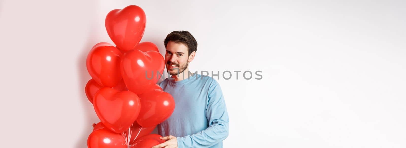 Romantic boyfriend bring red hearts balloons on Valentines day, surprise lover on date, standing over white background.