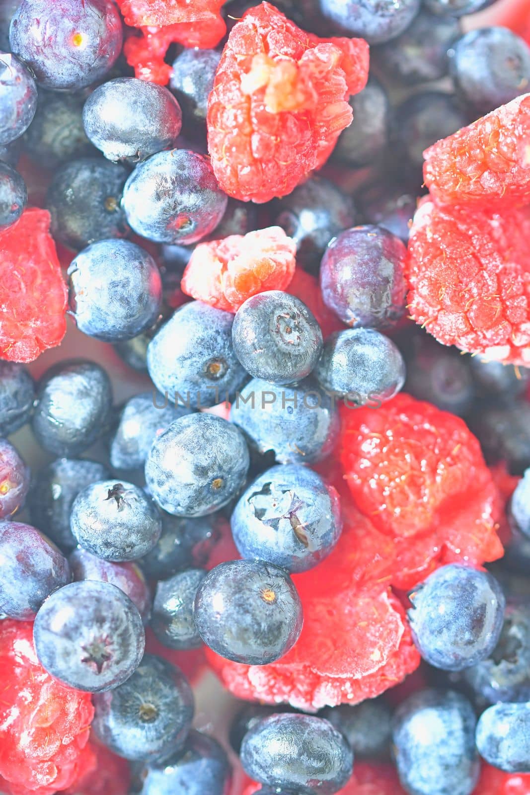 Frozen fresh blueberries and raspberries, close-up. Close-up view of bilberries and raspberries. Texture of frozen berries. Flat design, top view. Vertical image by roman_nerud