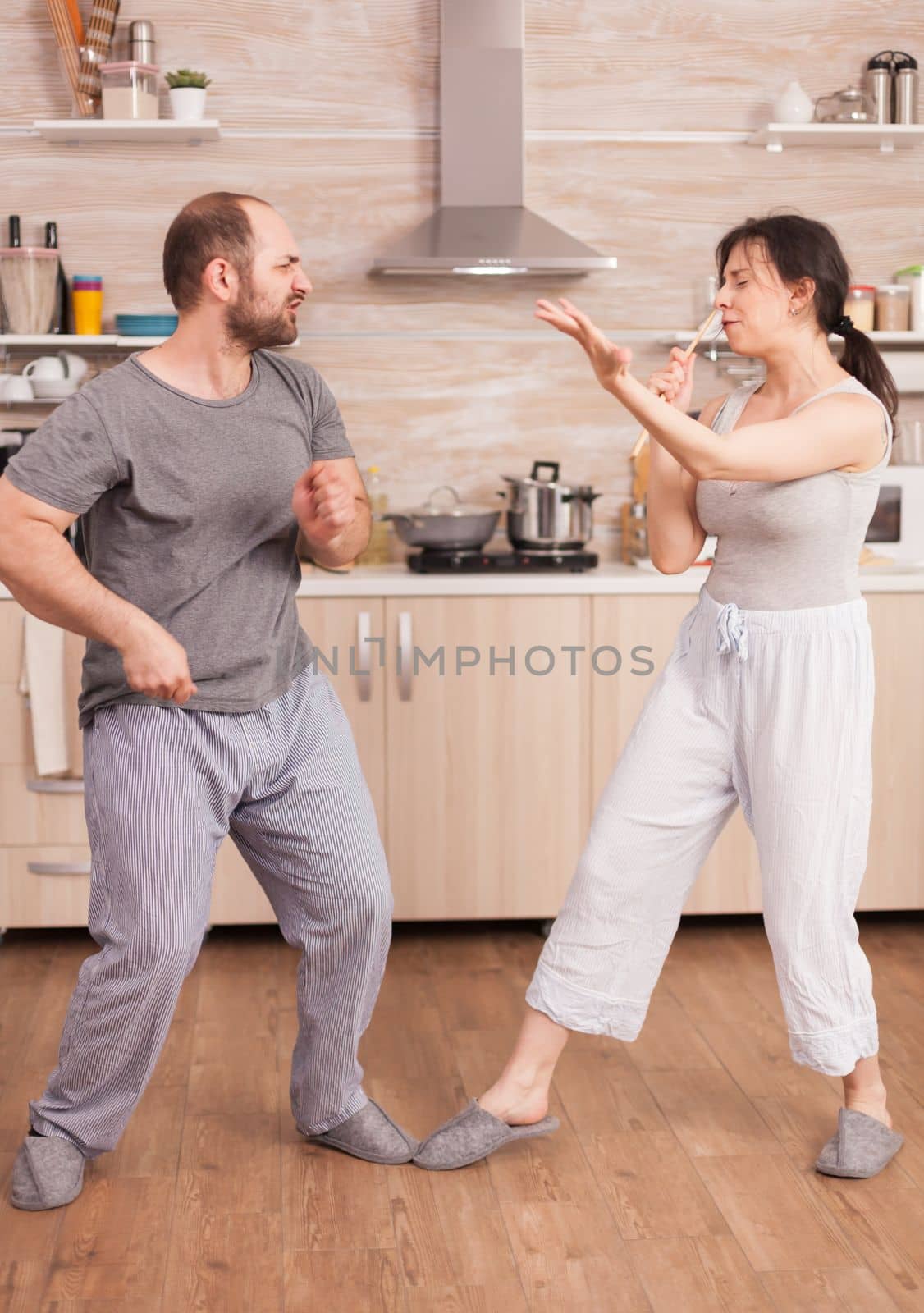 Positive cheerful crazy couple singing and dancing while having breakfast in kitchen wearing pajamas. Carefree wife and husband laughing having fun funny enjoying life authentic married people positive happy relation