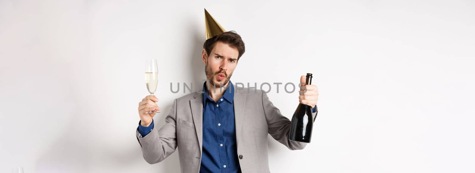 Celebration and holidays concept. Happy man in suit having fun at party, wearing birthday hat, dancing with champagne and drinking alcohol.