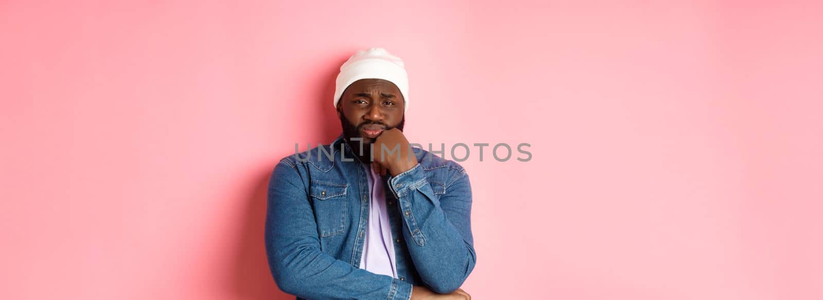 Young african-american man look with pity and concern at camera, frowning and feeling uneasy, standing over pink background.