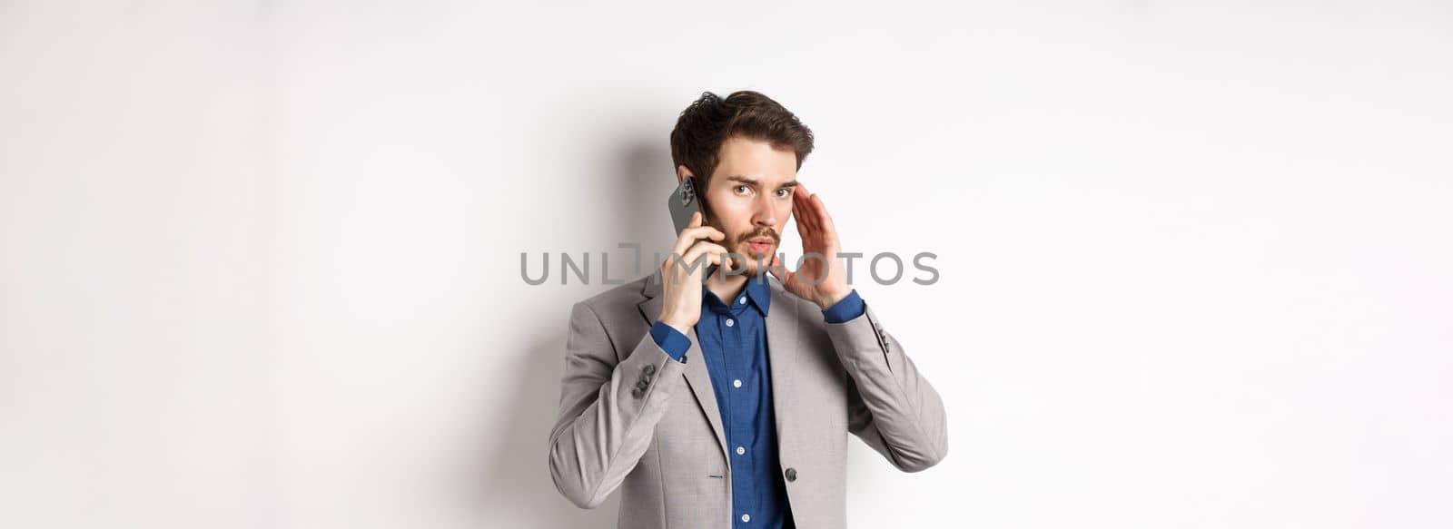 Businessman talking on phone and covering ear, receive call in loud place, cant hear caller, standing on white background.