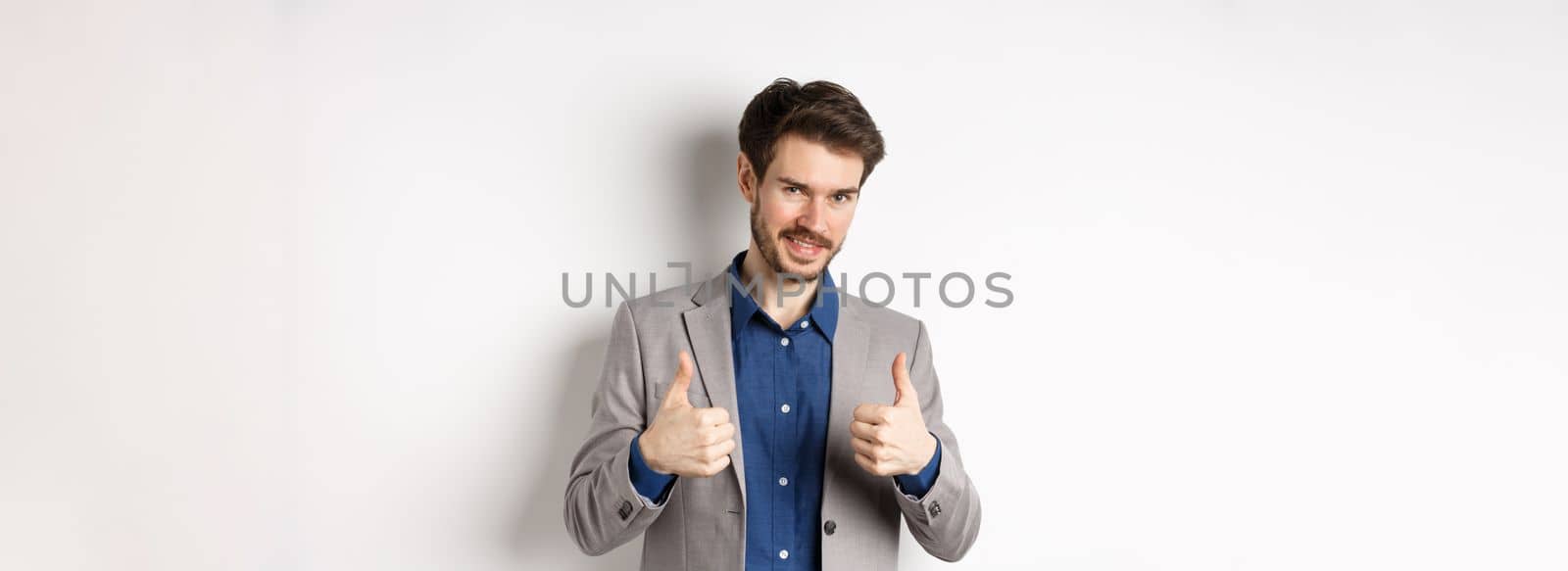 Very good. Smiling handsome male ceo manager showing thumbs up in approval, look proud and satisfied, say yes, approve nice work, standing on white background.