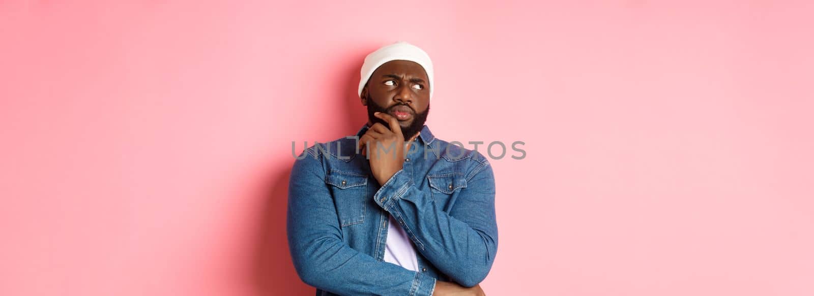 Doubtful african american man staring at upper left corner thoughtful, making decision and thinking, standing over pink background.