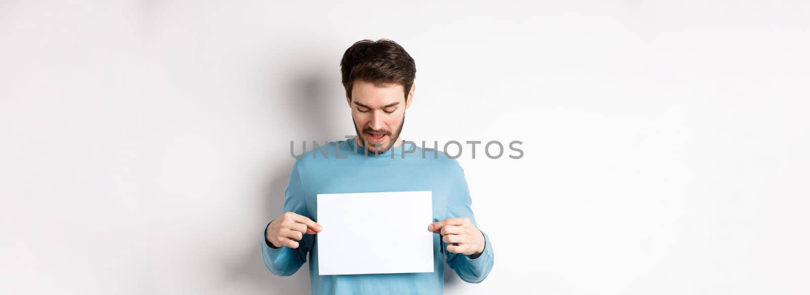 Excited bearded guy reading banner on blank piece of paper, showing logo, standing over white background.