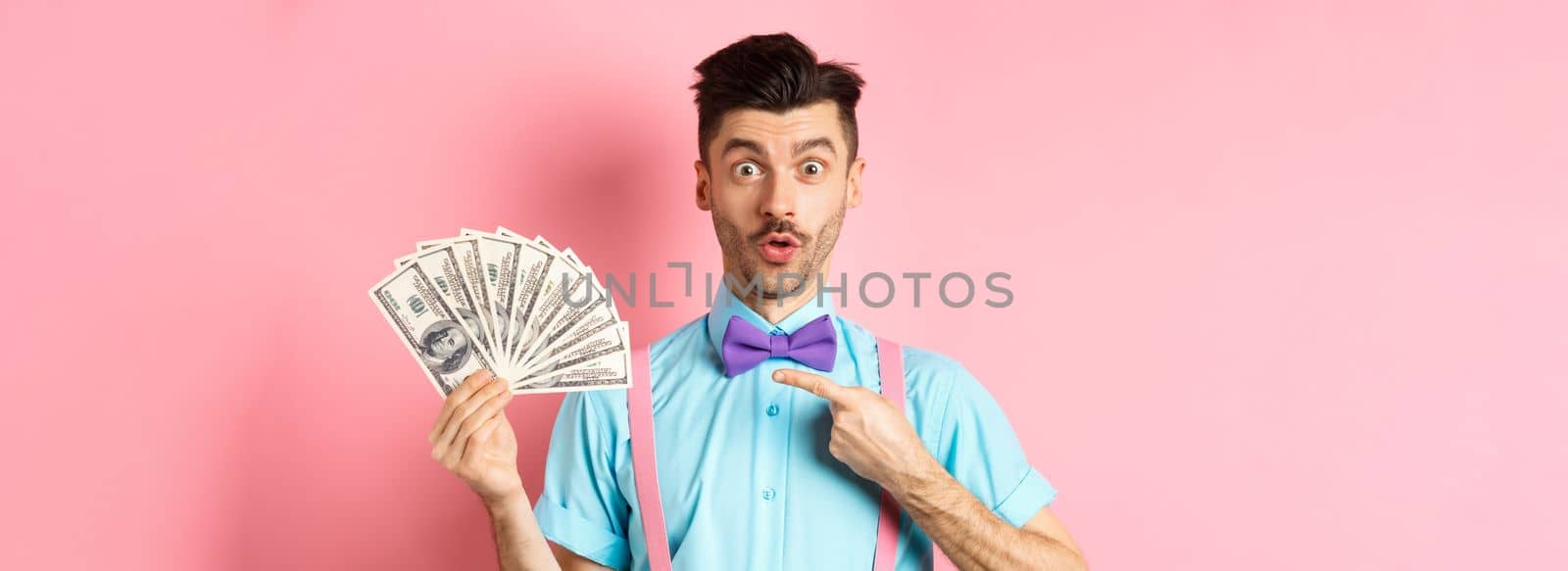 Amazed man showing big money prize, pointing at dollars and say wow, stare impressed at camera, standing over pink background by Benzoix