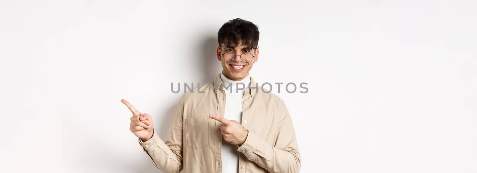 Handsome caucasian man in glasses smiling, pointing fingers at upper right corner, showing logo on white background by Benzoix