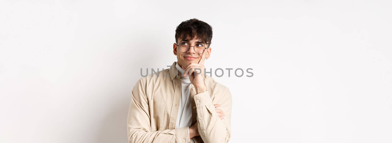 Image of happy dreamy young man imaging something good, smiling and looking at upper right corner thoughtful, standing on white background.