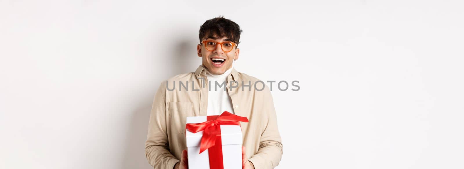 Surprised happy guy receiving a gift, holding present box and smiling amazed, standing on white background by Benzoix