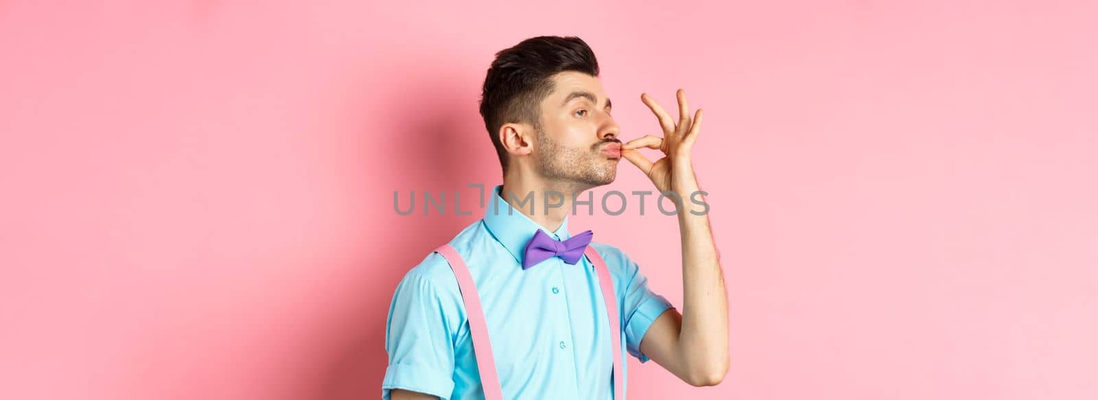 Profile of funny guy touching his french moustache and pucker lips like snob, standing smug on pink background and look left.