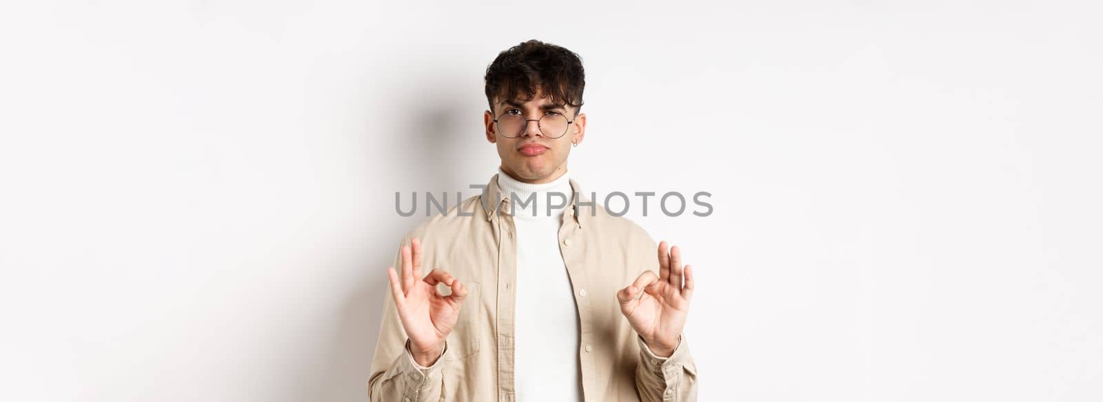 Not bad. Satisfied young man showing okay gestures and nod in approval, praise good work, pleased with results, standing on white background.