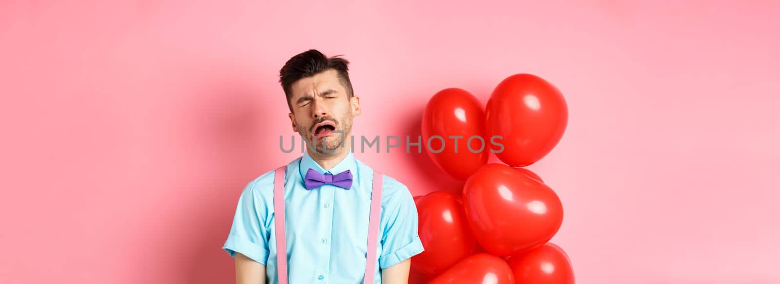 Valentines concept. Sad and heartbroken man crying over break-up, being cheated on lovers day, sobbing and feeling lonely, standing on pink background.