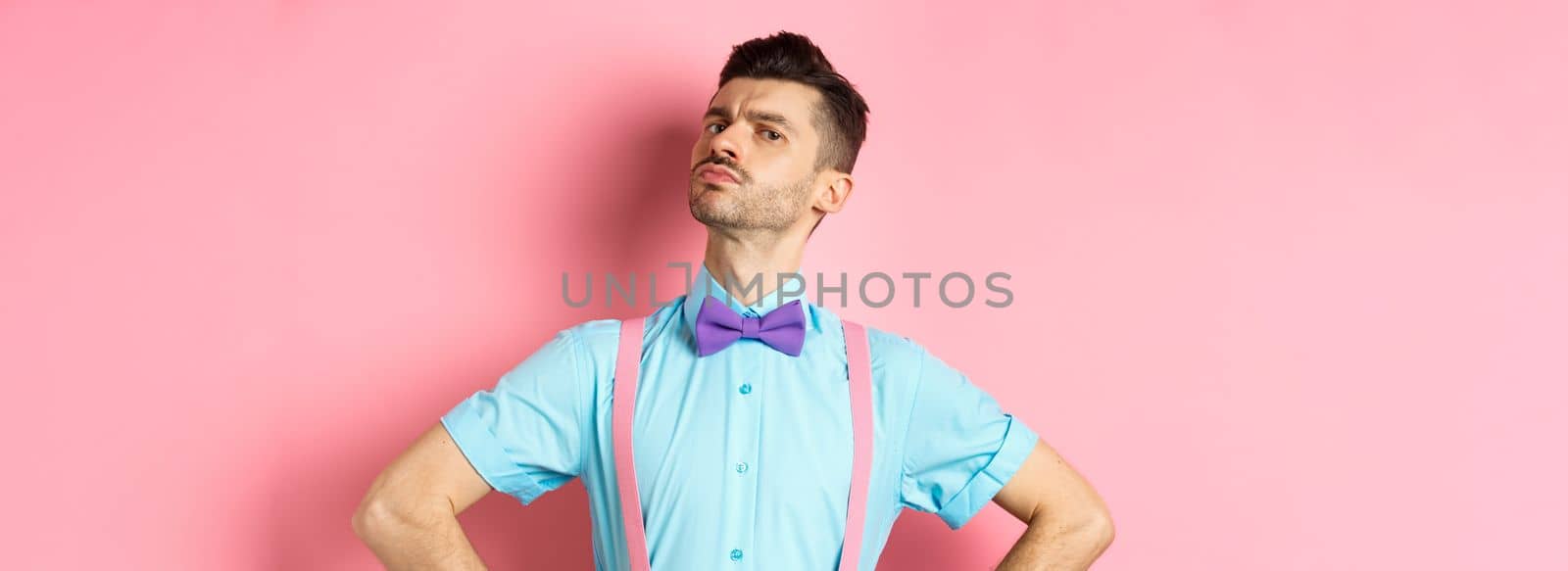 Proud and confident caucasian guy with moustache and bow-tie, looking arrogant with chin up, frowning and looking at camera, standing on pink background by Benzoix