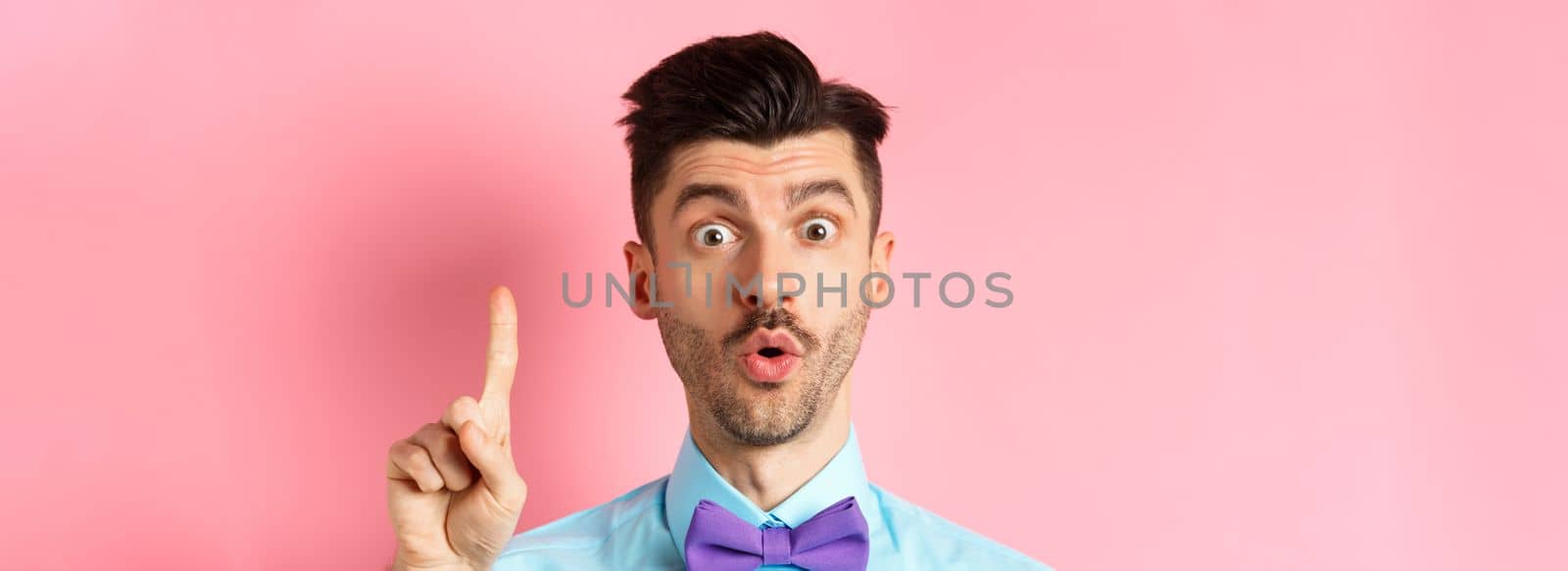 Close-up of excited funny guy with moustache and bow-tie, pitching an idea, raising finger to say suggestion, have plan, standing over pink background.