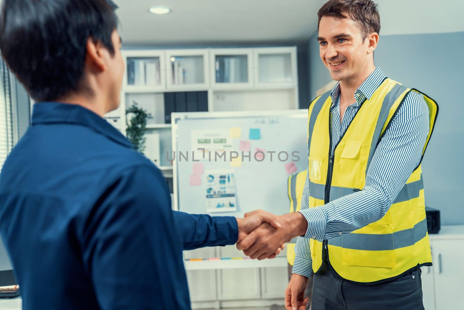 An engineer with a protective vest handshake with an investor in his office. Following a successful meeting, employee and employer form a partnership.