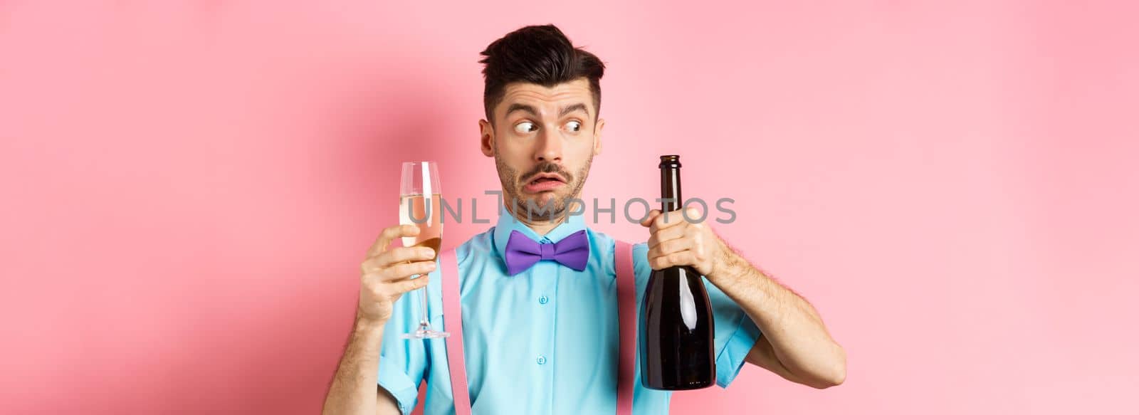Holidays and celebration concept. Confused drunk guy looking at empty bottle of champagne, holding glass, drinking at party, standing over pink background by Benzoix