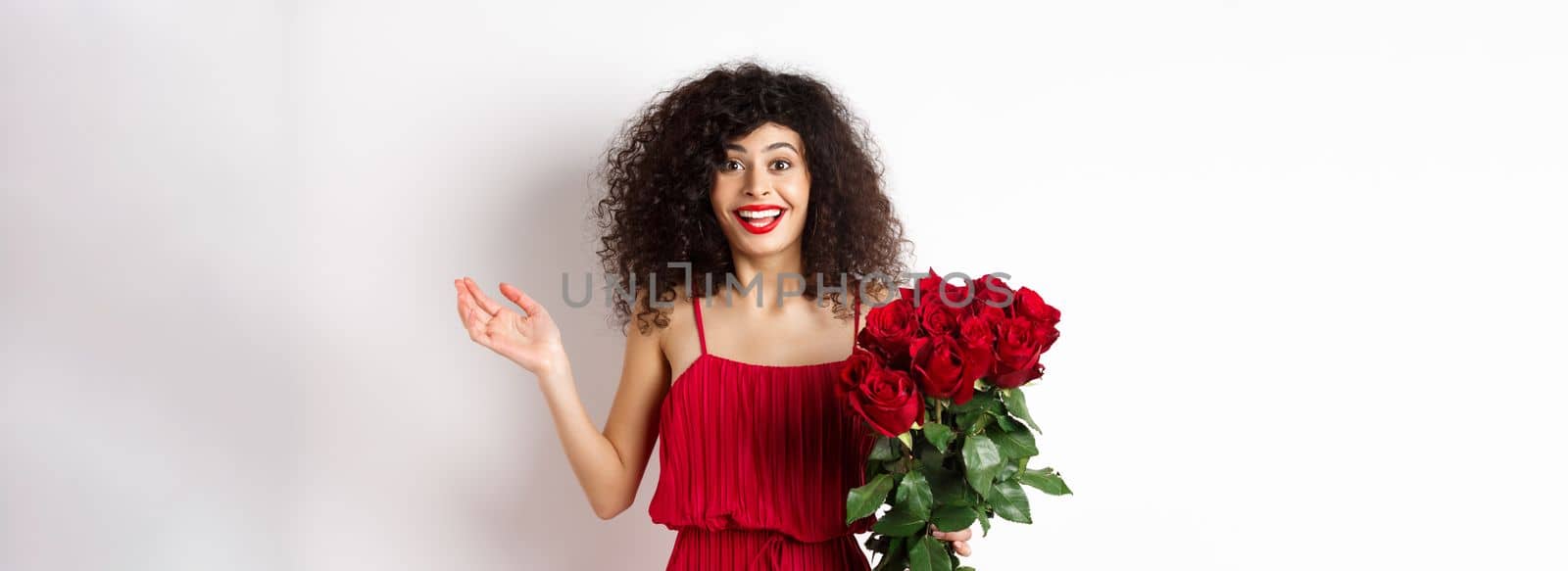 Romance and Valentines day. Woman gasping surprised and happy, receive surprise gift from lover, holding bouquet of red roses, standing on white background.