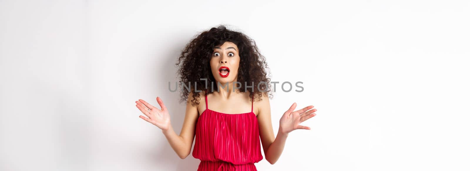 Excited woman with curly hair, talking with amazed face, explain big news, shaking hands and look astonished at camera, white background by Benzoix