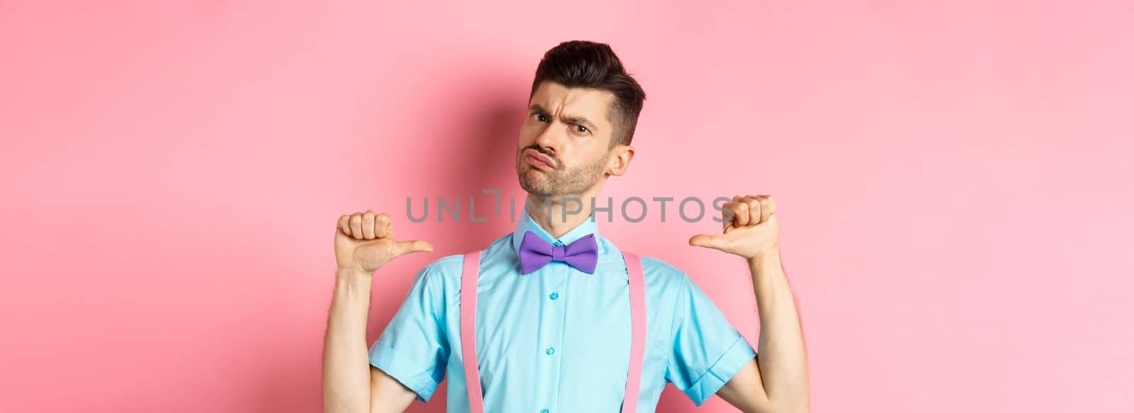 Serious and funny young man trying look cool, pointing at himself to self-promote, being a professional, standing over pink background by Benzoix