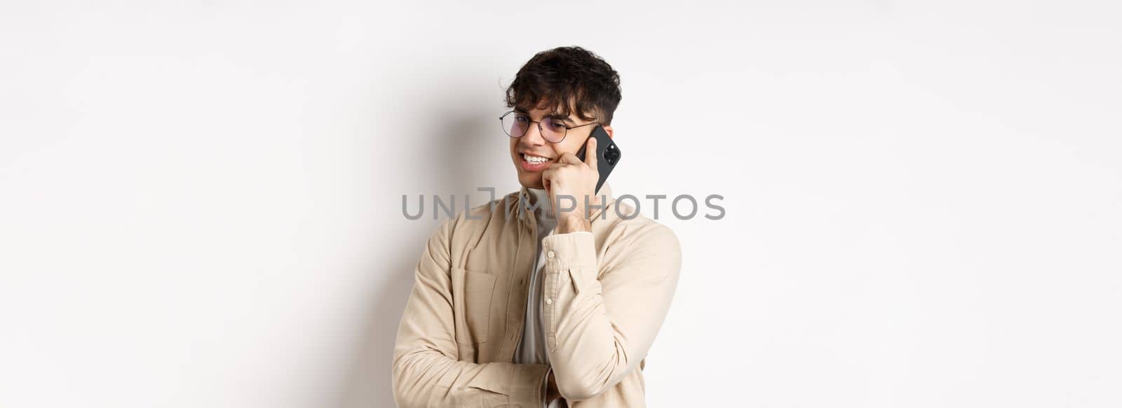 Real people concept. Handsome modern man talking on mobile phone, look aside and holding smartphone near ear, standing on white background by Benzoix