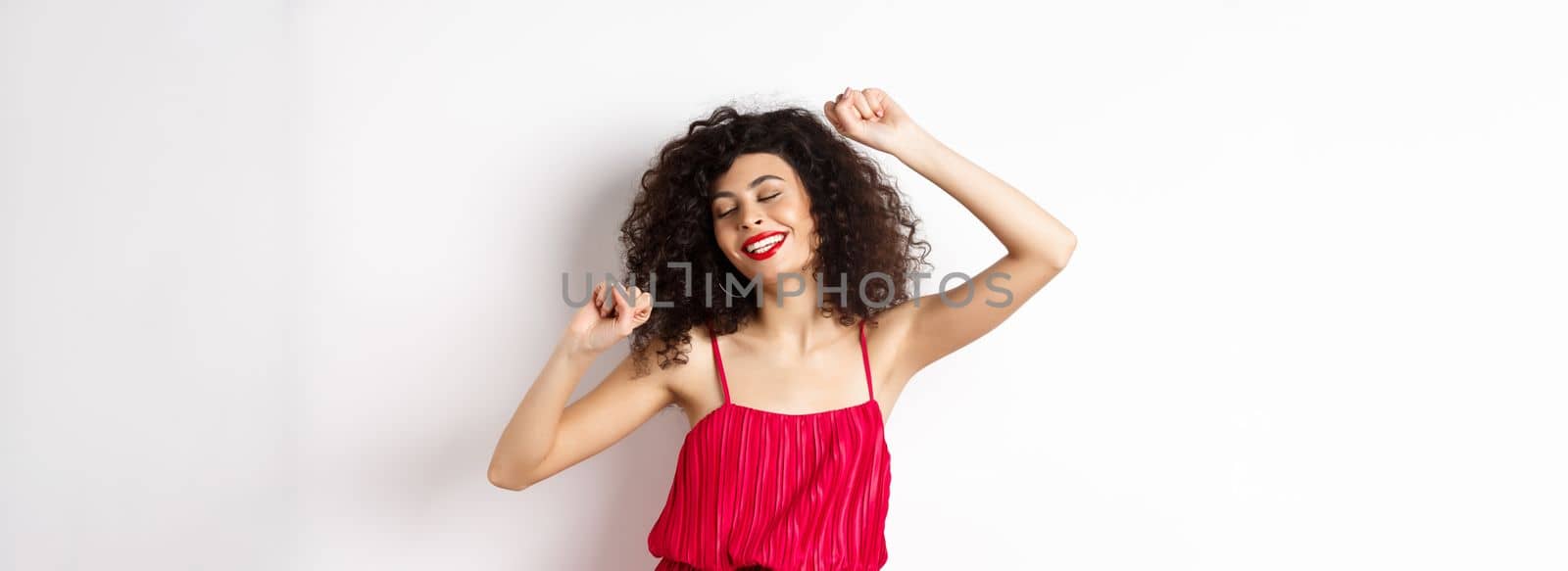 Happy elegant woman in red dress dancing on white studio background.