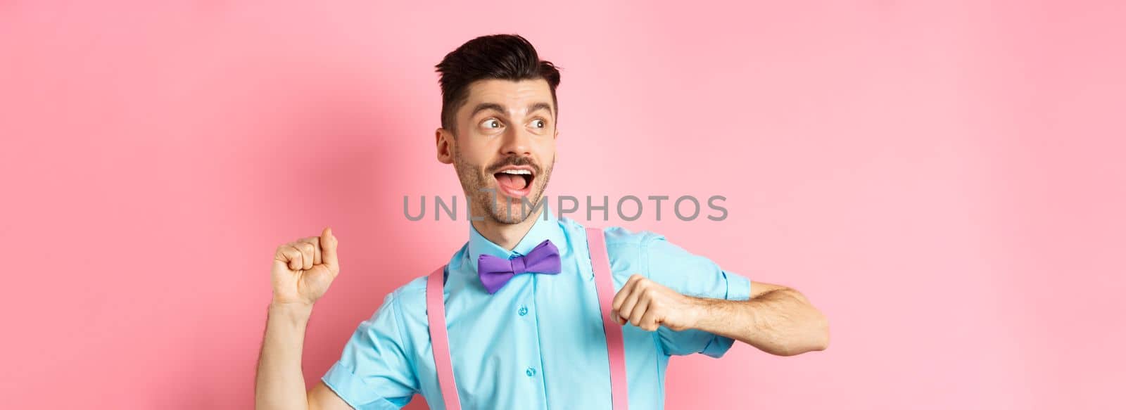 Portrait of funny young guy hurry up and running, looking aside with excited face, rushing to get promo offer, standing over pink background.