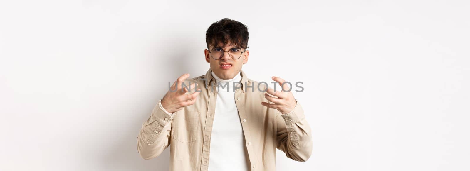 Portrait of annoyed and mad guy wants to strangle someone, grimacing from hatred and clench arms, standing bothered on white background by Benzoix