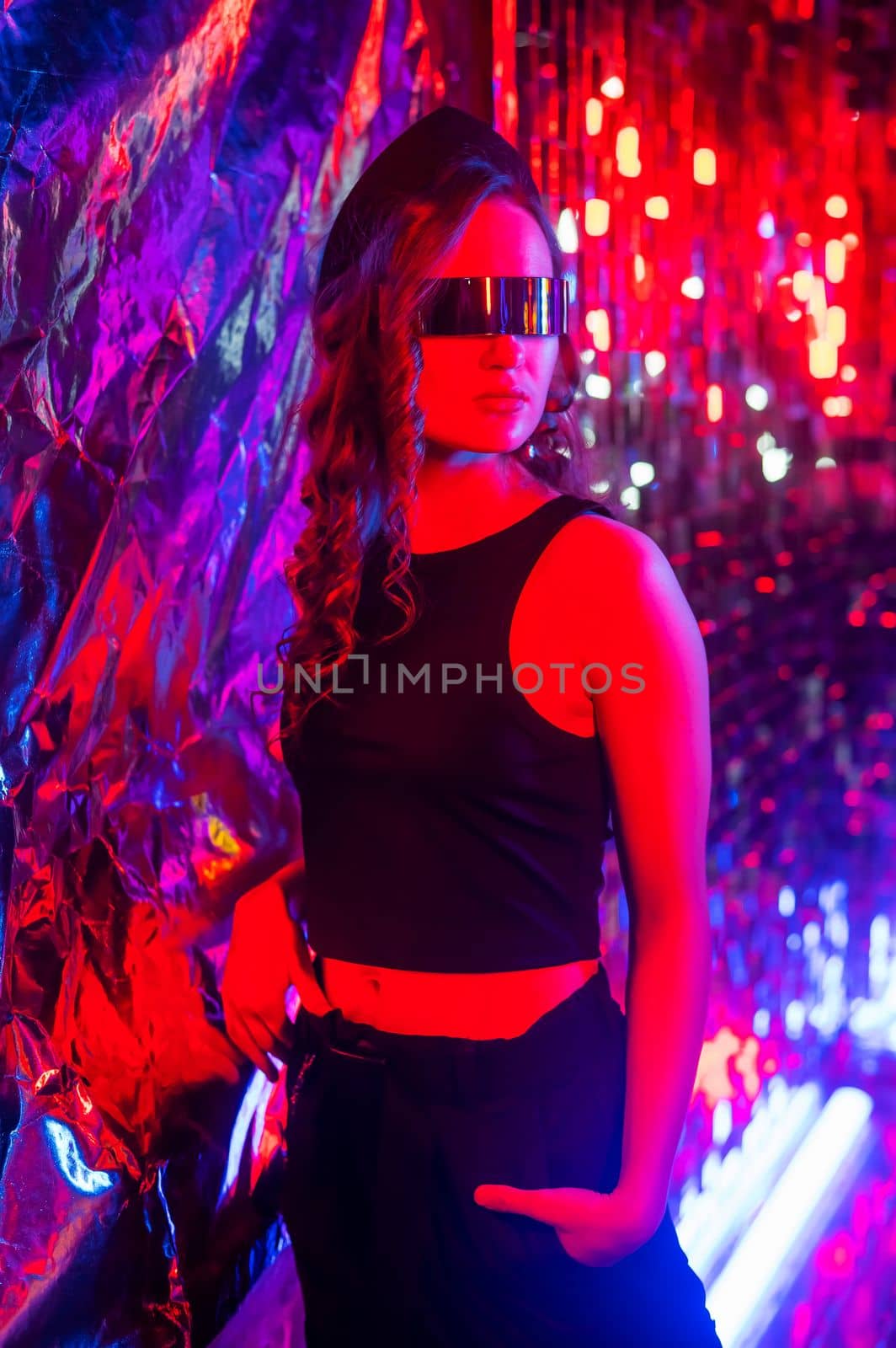 Close-up portrait of caucasian woman in sunglasses in neon light against foil wall