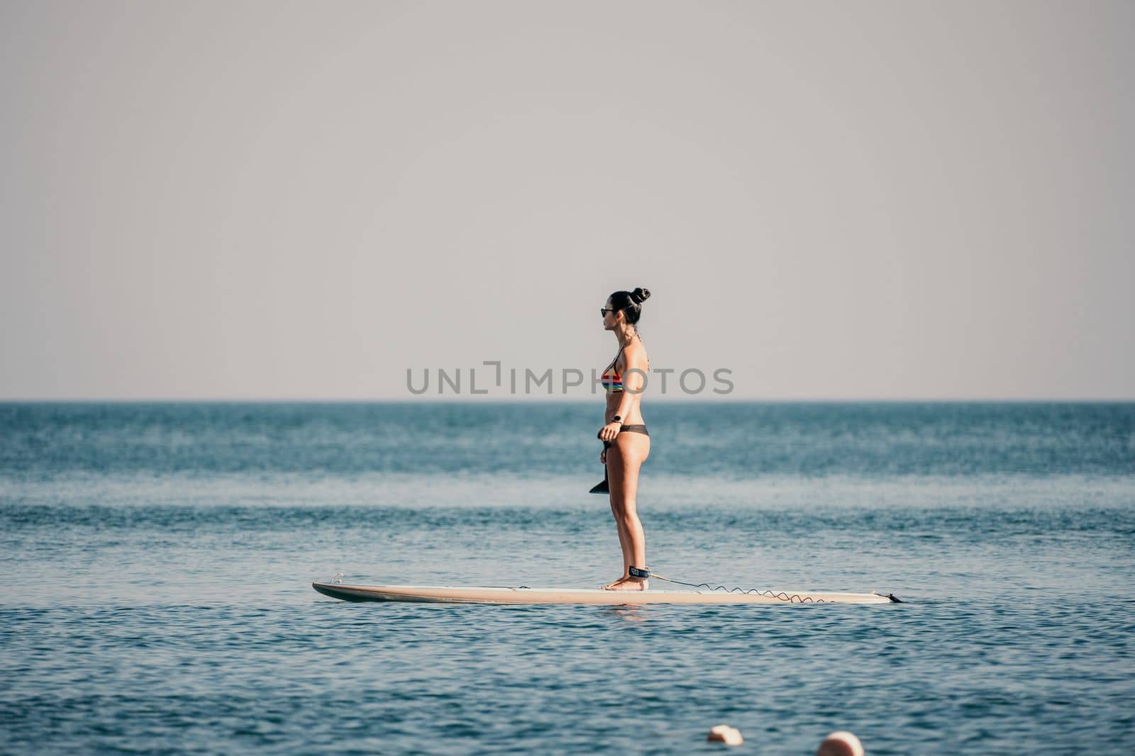 Sea woman sup. Silhouette of happy middle aged woman in rainbow bikini, surfing on SUP board, confident paddling through water surface. Idyllic sunset. Active lifestyle at sea or river