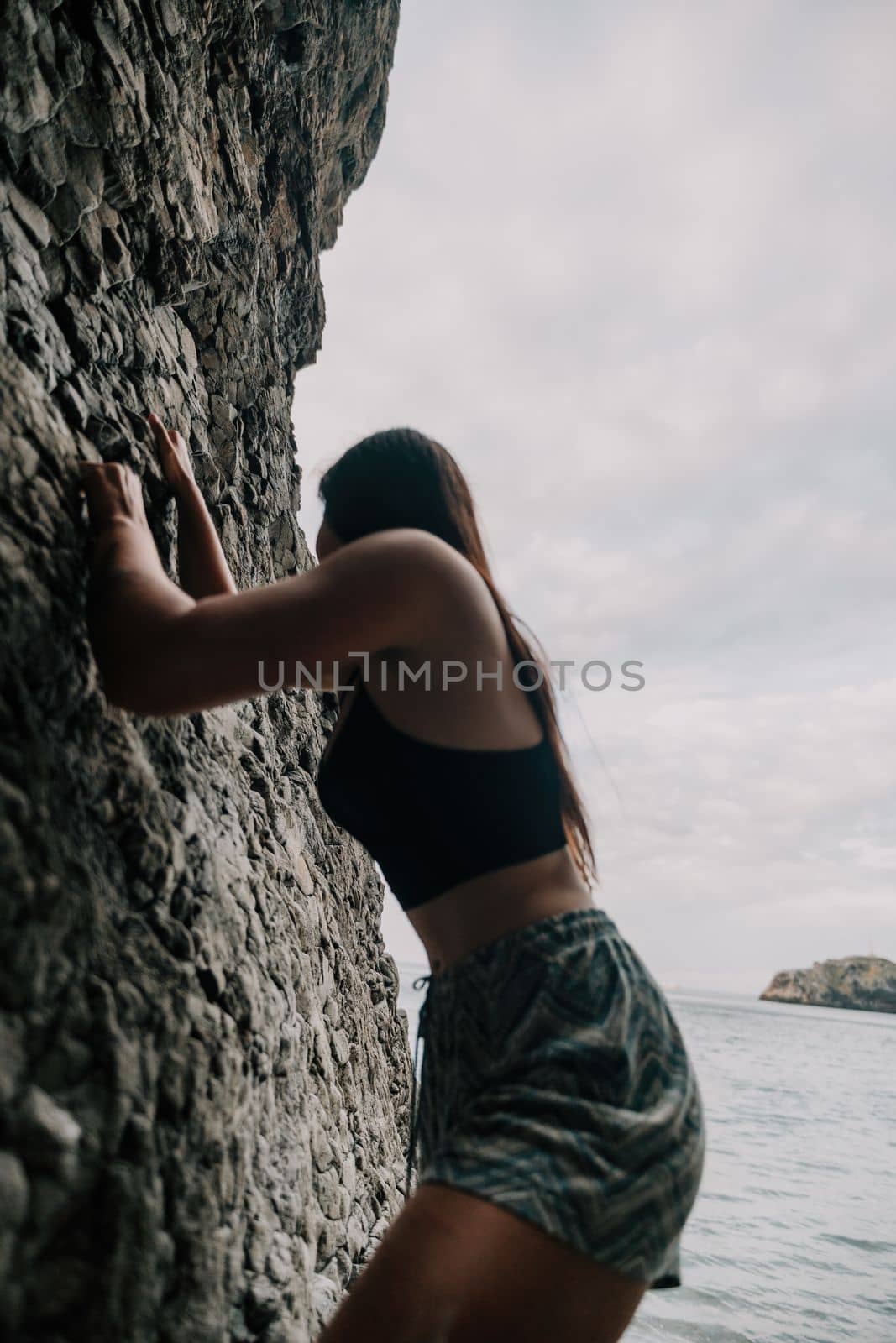 A girl climbs a rock. The athlete trains in nature. Woman overcomes difficult climbing route. Extreme hobby. Tourist woman rock climber hiking on mountains rocks over beautiful sea coast