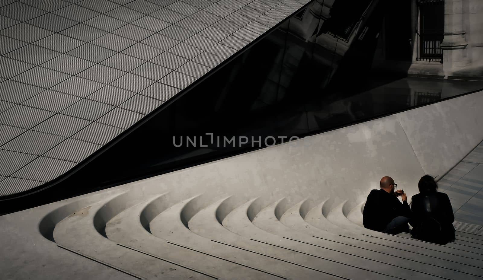 London, England - Apr 21, 2019 : Two men sit leisurely on cemented stairs in front of the west entrance to the Victoria and Albert Museum. Rear view, Selective focus.