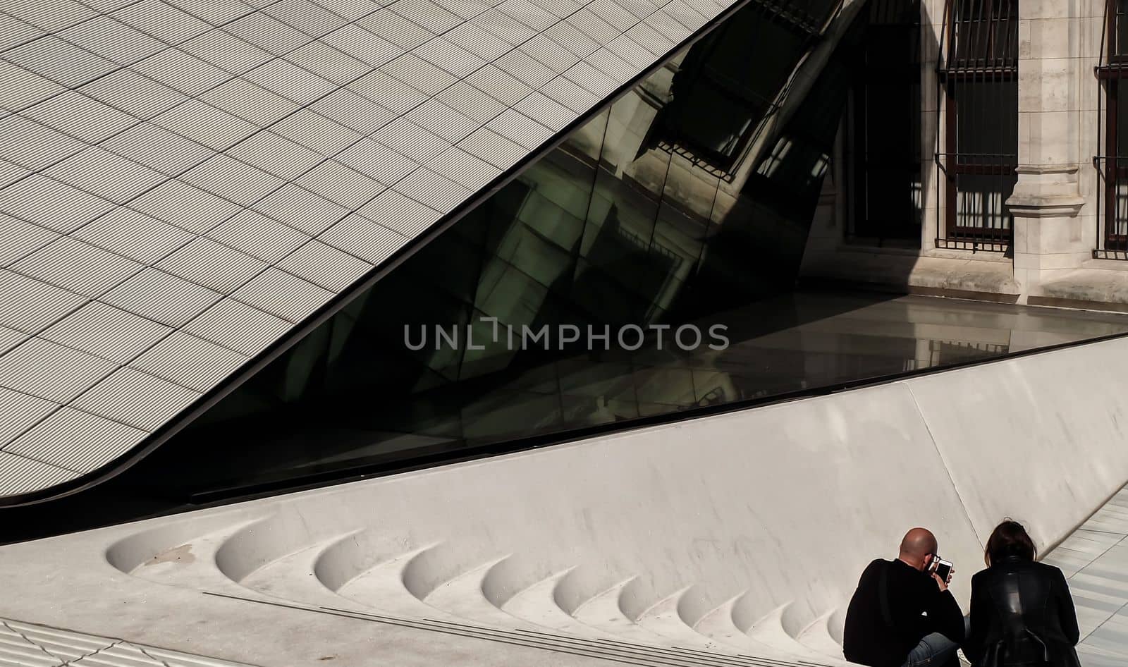 London, England - Apr 21, 2019 : Two men sit leisurely on cemented stairs in front of the west entrance to the Victoria & Albert Museum. Rear view, Selective focus.