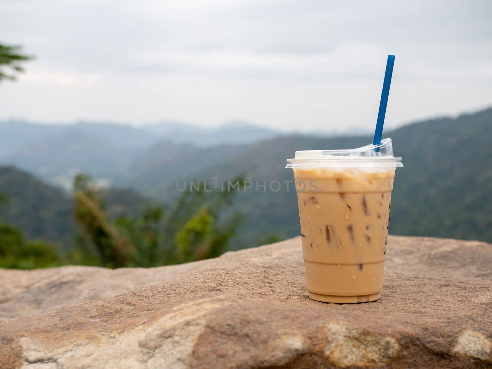 A glass of iced coffee is placed on a rock against a background of mountains and sky.