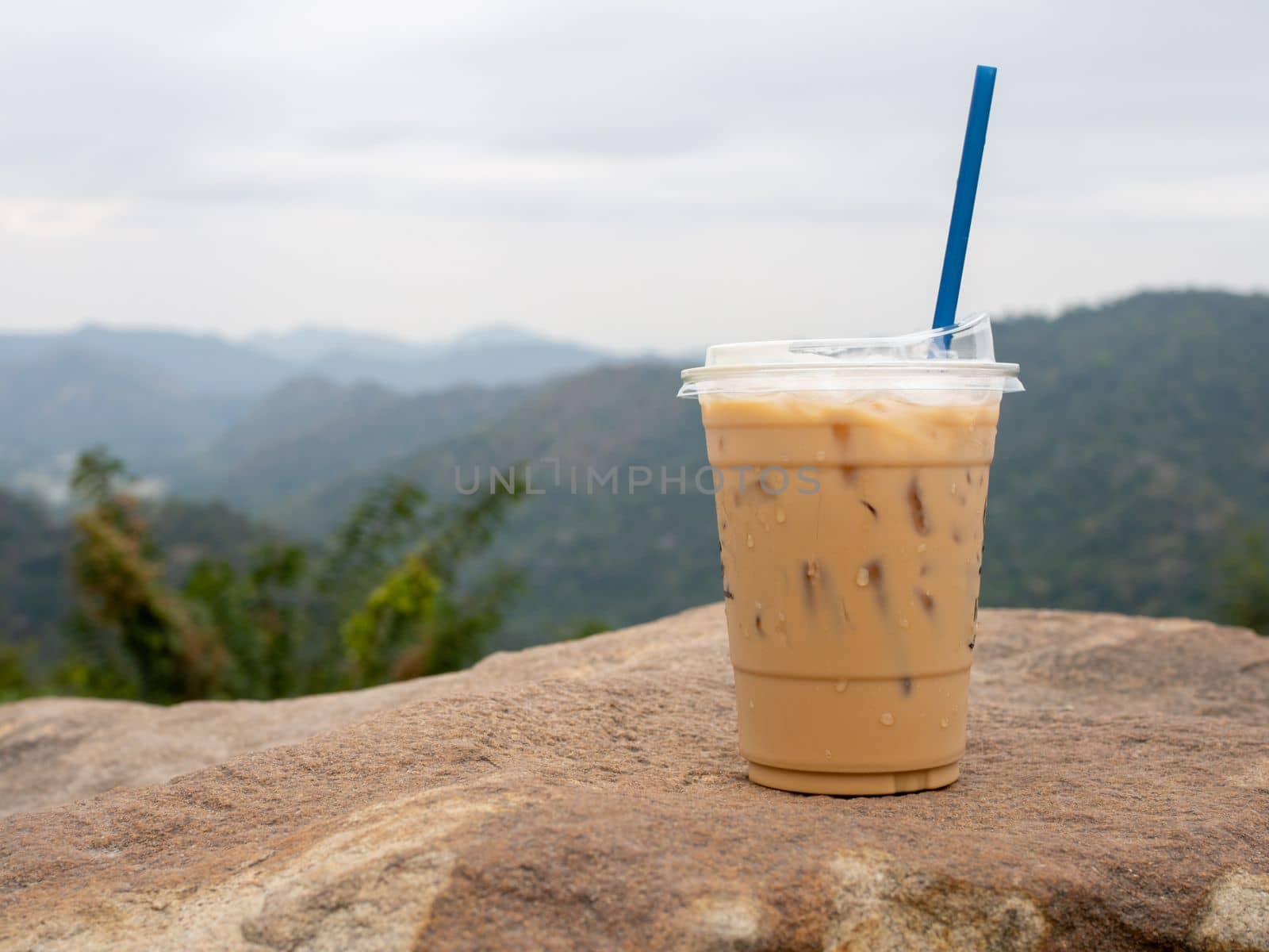 A glass of iced coffee is placed on a rock against a background of mountains and sky.