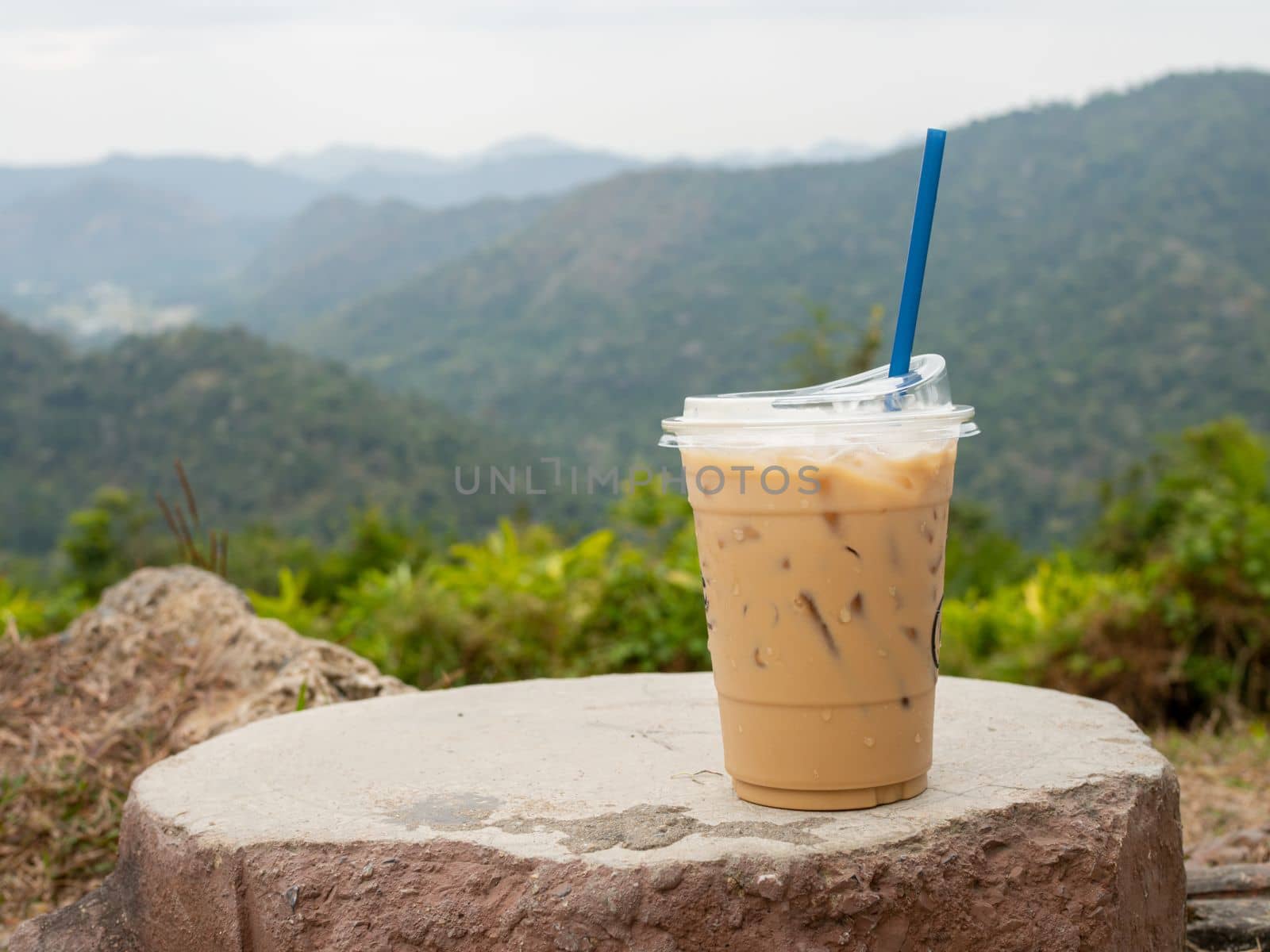 A glass of iced coffee is placed on a rock against a background of mountains and sky.