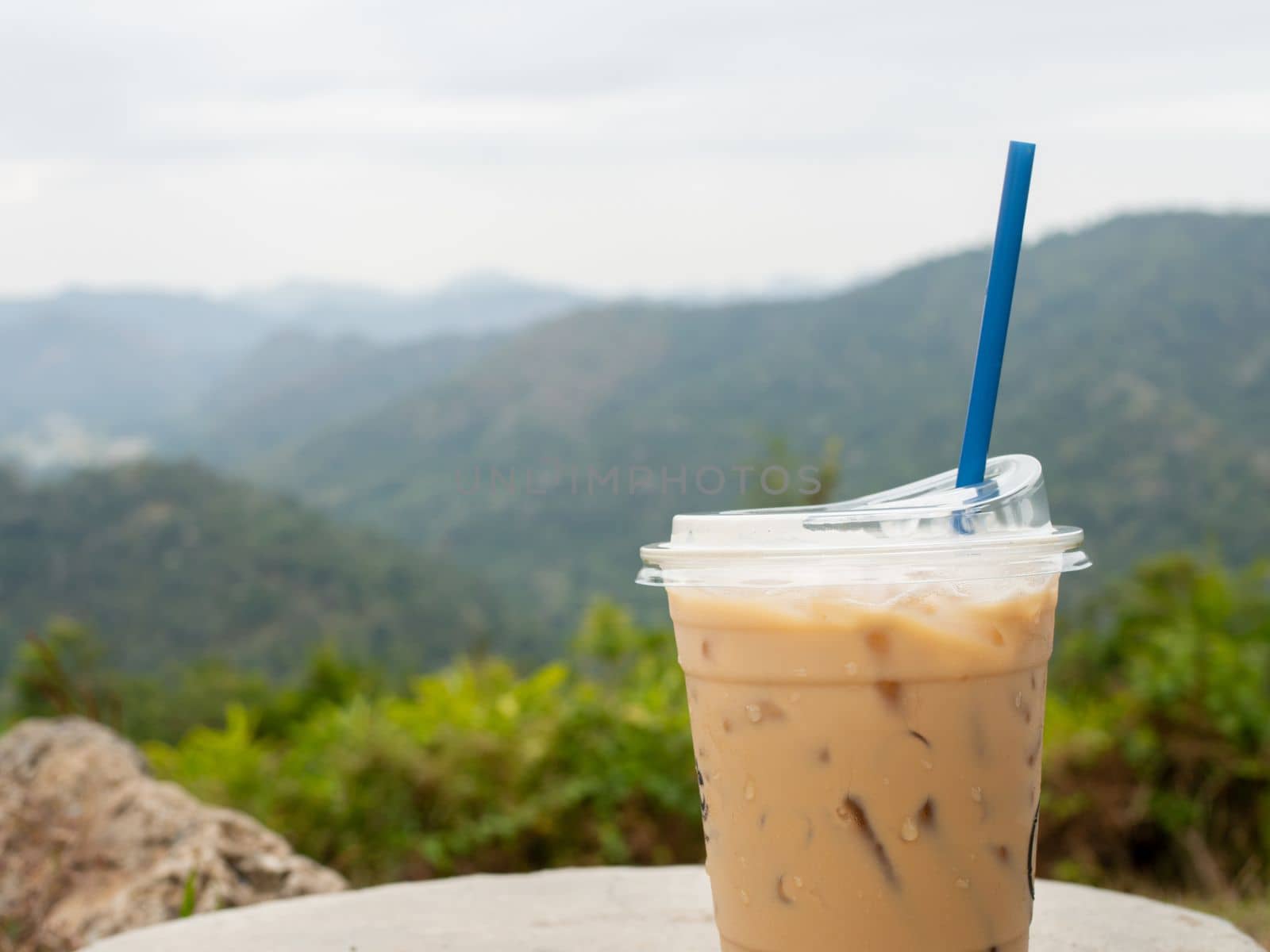 A glass of iced coffee is placed on a rock against a background of mountains and sky.