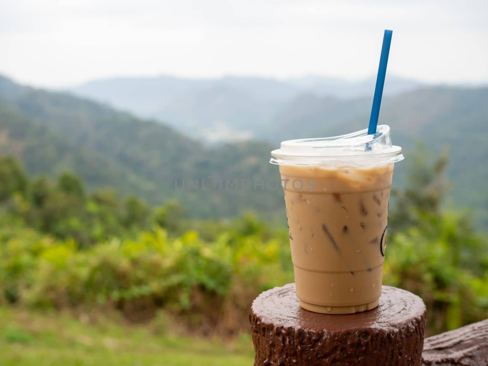 A glass of iced coffee is placed on the fence against a backdrop of mountains and sky.