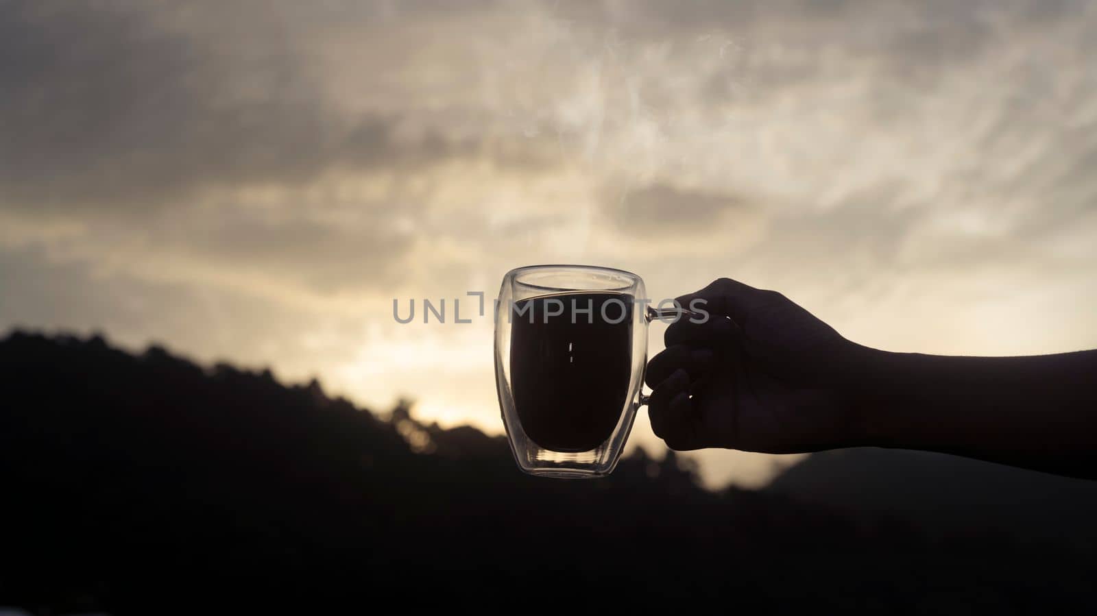 Silhouette of man holding coffee cup with beautiful natural mountain views in background.