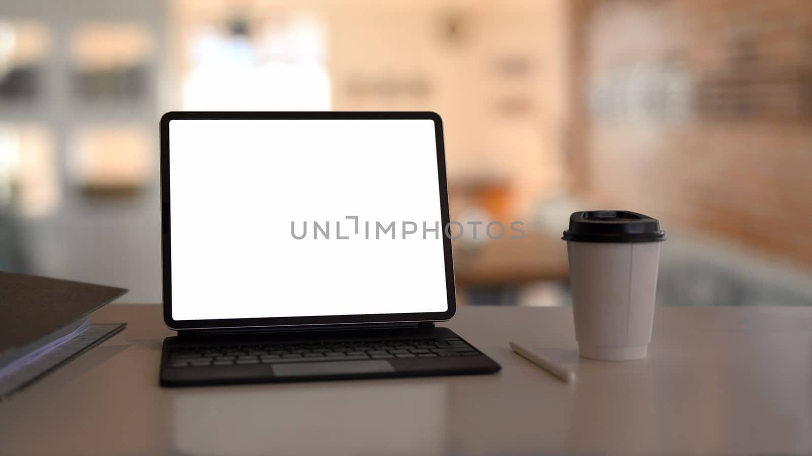 Computer tablet with blank display and coffee cup on white table.
