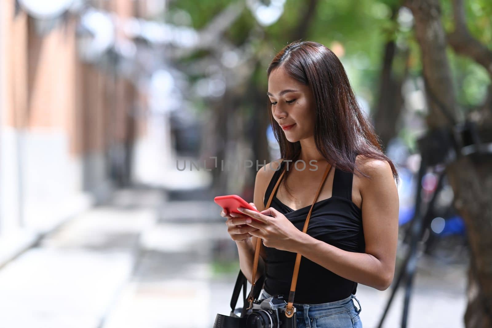 Young cheerful woman standing on the city street and using smart phone.