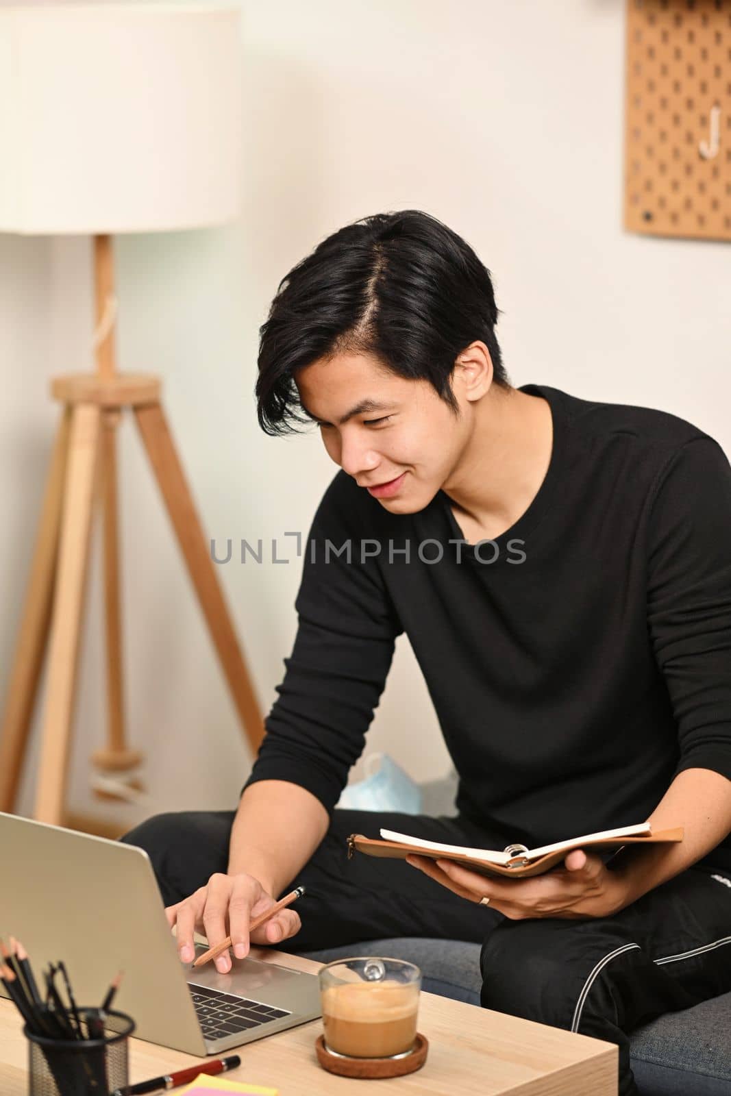 Young man holding book and using laptop computer in living room. by prathanchorruangsak