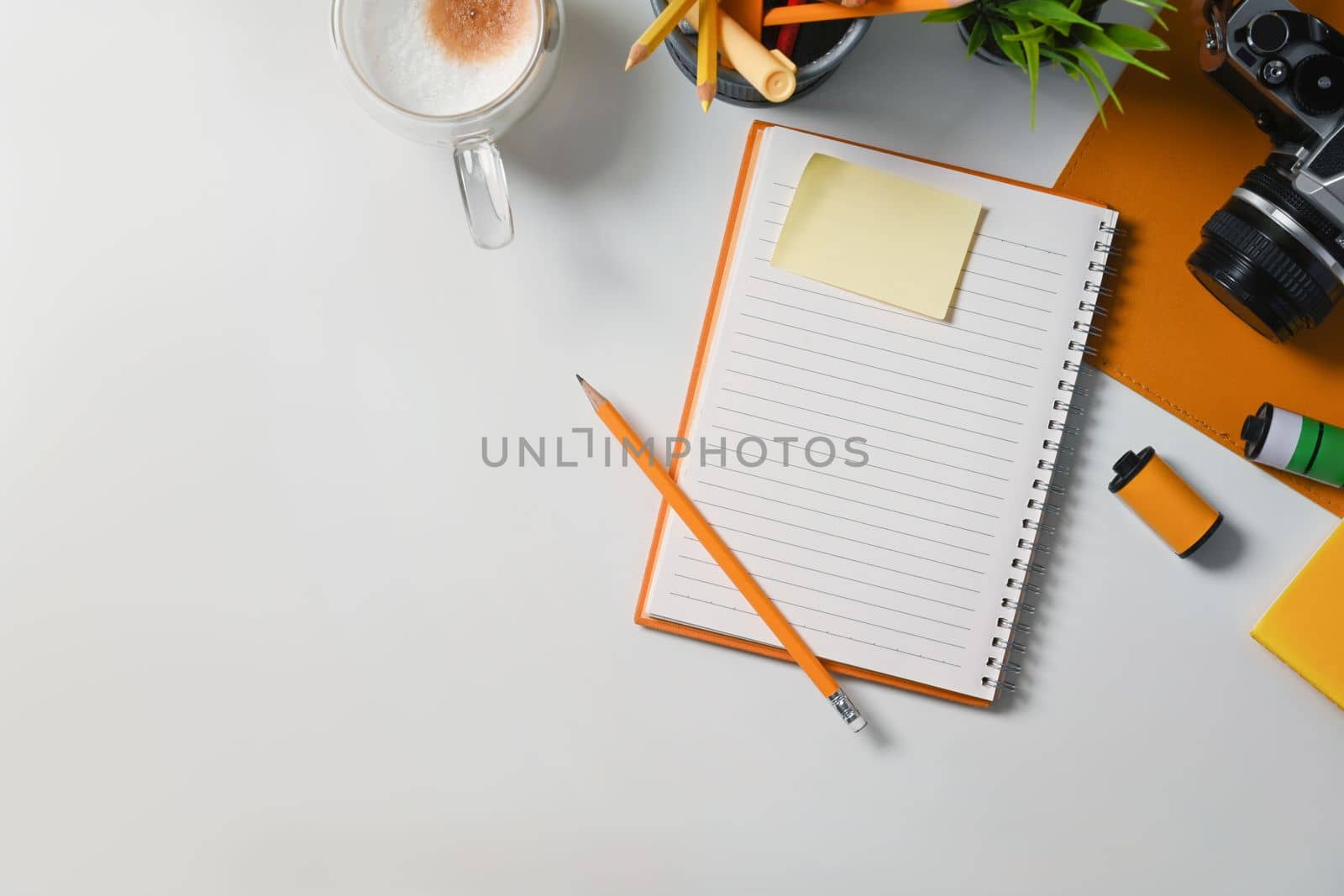 Above view empty notebook, sticky note, coffee cup and camera on white table. by prathanchorruangsak
