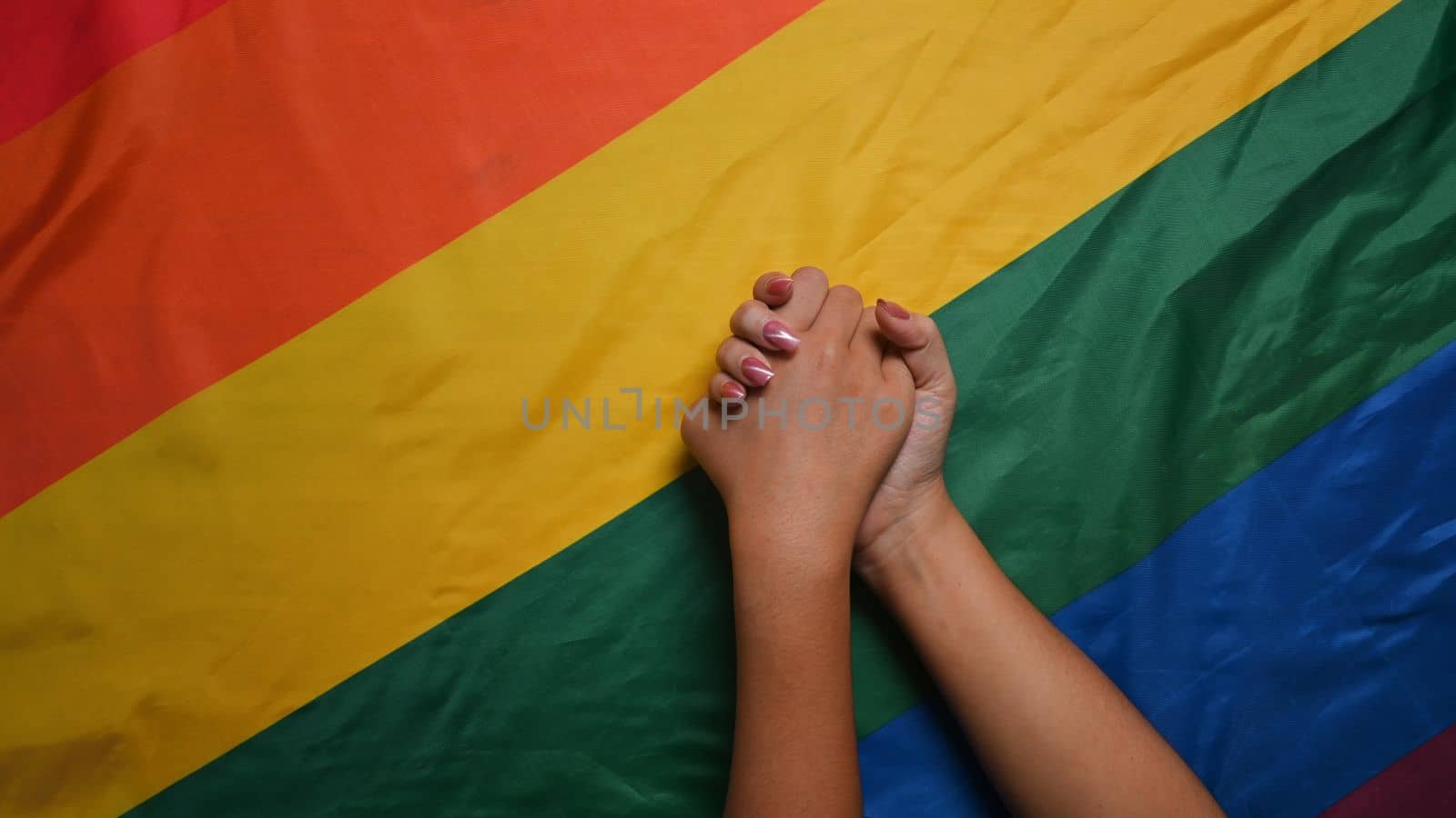 Young asian women LGBT lesbian couple holding hands over LGBT pride flag. by prathanchorruangsak