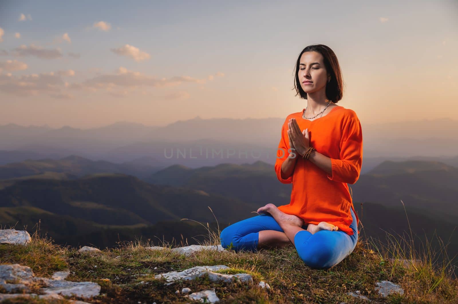 A young woman practices yoga outdoors in a beautiful mountain landscape. Against the background of sunsets, lotus position and namaste. Meditation and relaxation.