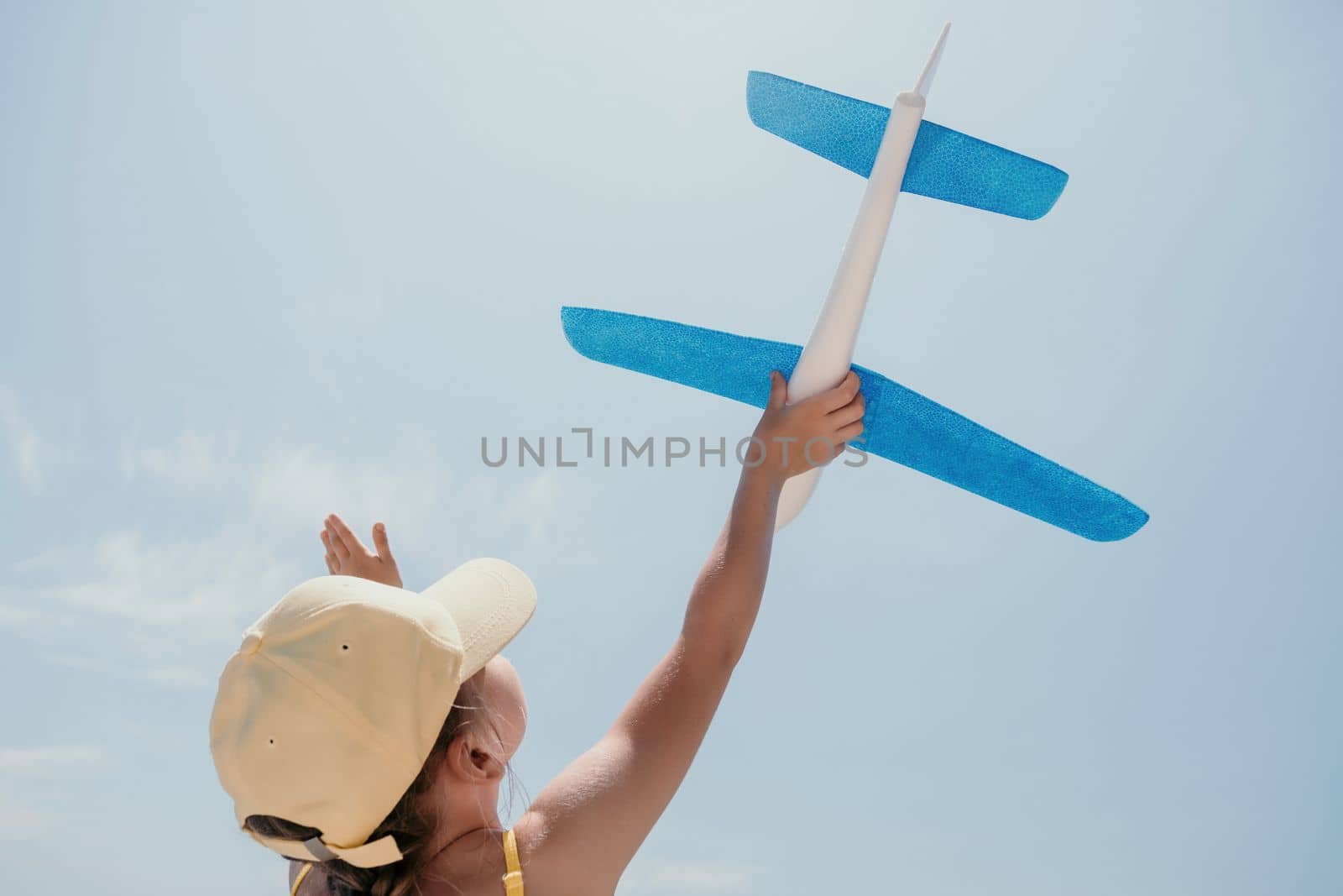 Kid playing with toy airplane. Children dream of travel by plane. Happy child girl has fun in summer vacation by sea and mountains. Outdoors activities at background of blue sky. Lifestyle moment. by panophotograph