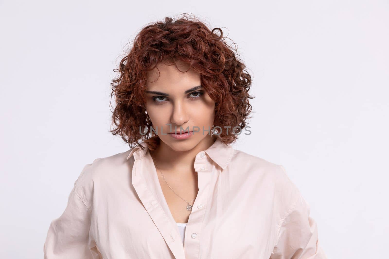 A nervous woman. She kills with her eyes. Natural hairstyle. Beautiful curly chestnut-colored hair. Hairstyle. Light-colored long-sleeved blouse.