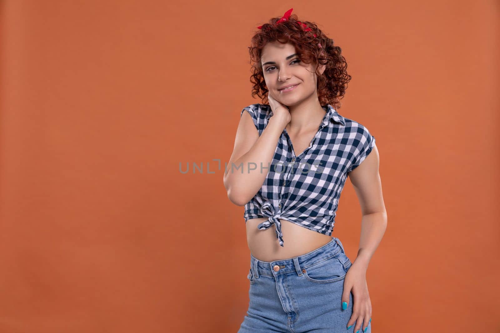 Pin up styling. Girl wearing plaid shirt and tied at the bottom. Short curly hair in chestnut color. Isolated from the uniform background.