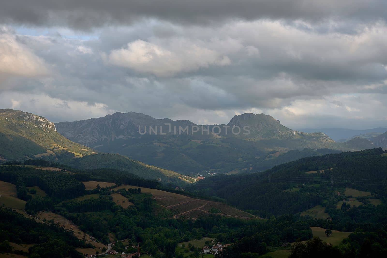 Rustic mountain landscape with cloudy sky.Bien Aparecida, Cantabria, meadows, trees and pastures for animals, rustic houses, sky with storm clouds.