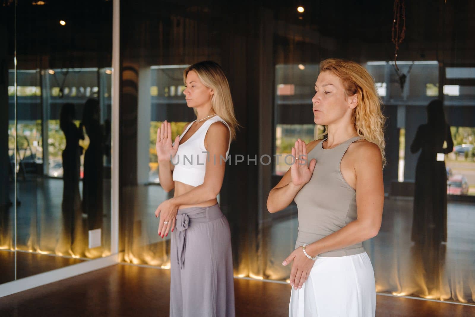 Two beautiful women are doing yoga standing up in the fitness room.